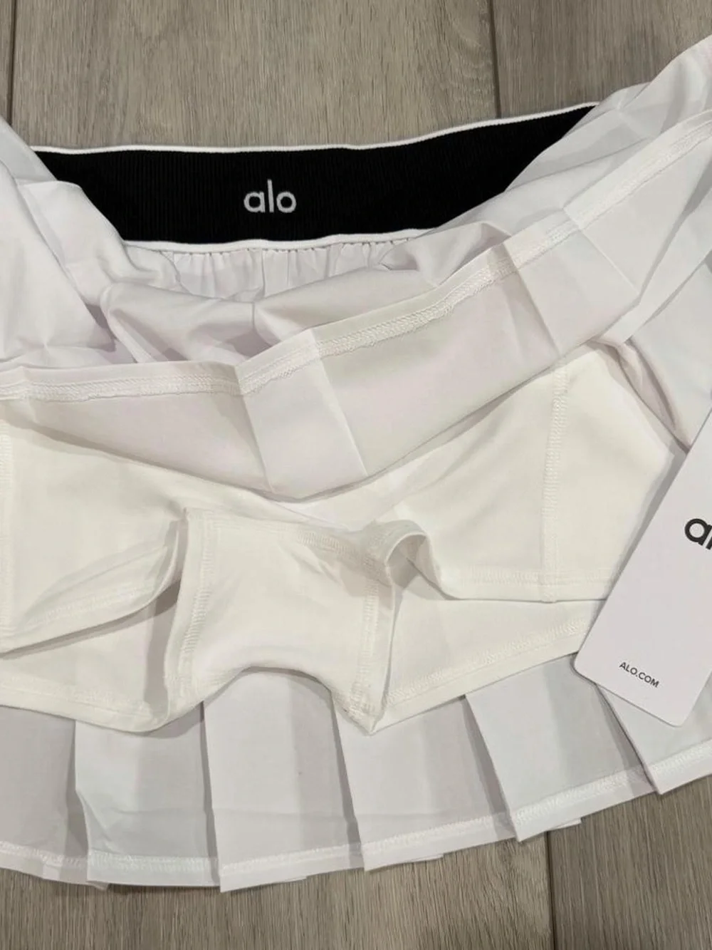 alo Yoga Low Rise AMP It Up Tennis Skirt in White with Black Waistband. SIZE: S